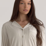 Muse Long PJs — Dusk: Woman in beige long-sleeved pajamas with white piping.