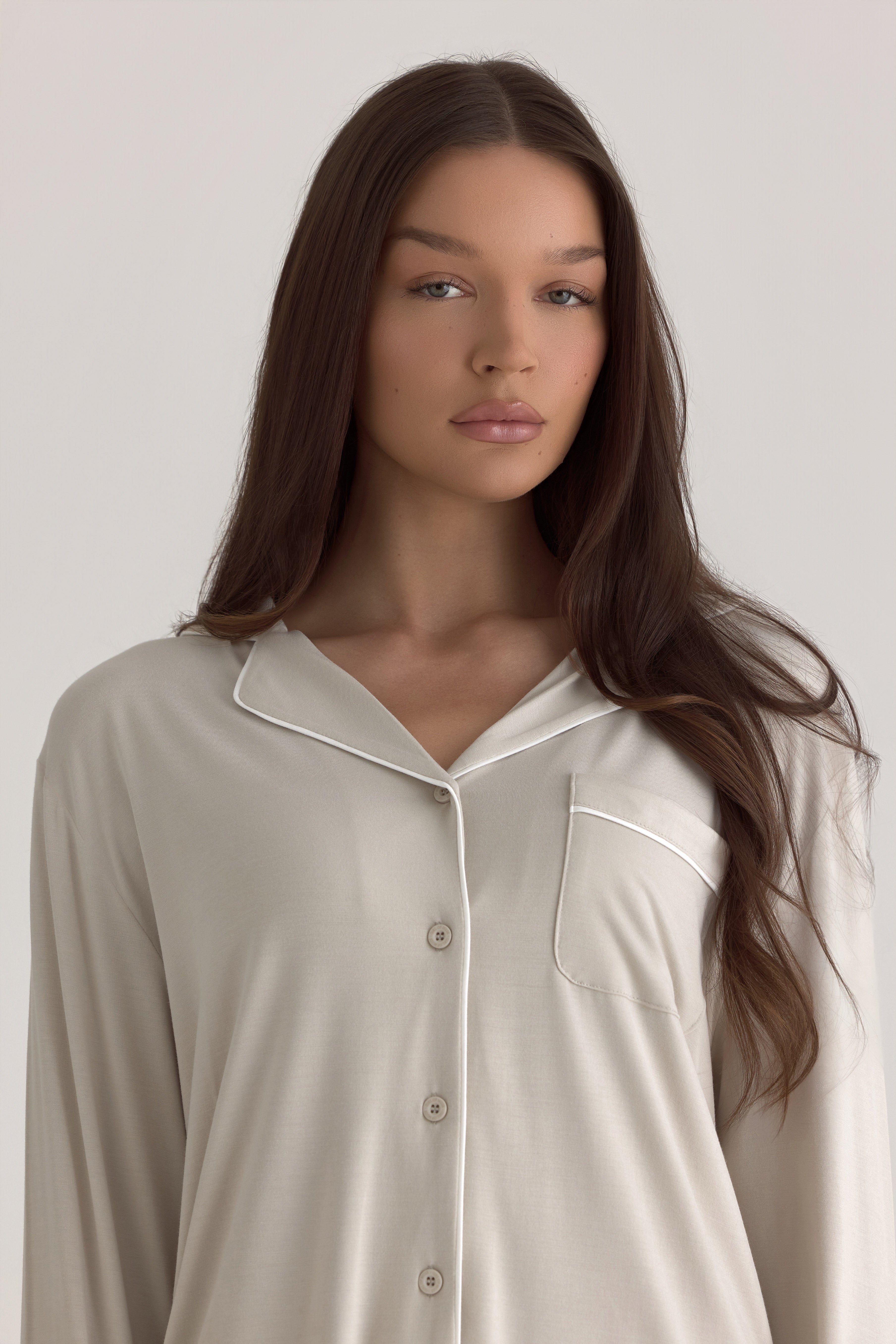 Muse Long PJs — Dusk: Woman in beige long-sleeved pajamas with white piping.