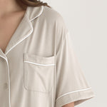 Muse Short PJs — Dusk:  Beige short-sleeve pajama set with white piping detail, featuring a collared shirt and chest pocket.
