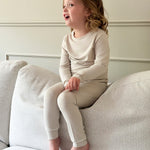 Mini Muse PJs — Dusk: Adorable toddler in beige long-sleeve pajamas sitting on a couch.