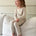 Mini Muse PJs — Dusk: Adorable toddler in beige long-sleeve pajamas sitting on a couch.