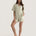 Muse Short PJs in Soft Sage: A woman models a comfortable sage green pajama set with short sleeves and shorts, featuring white piping detail.