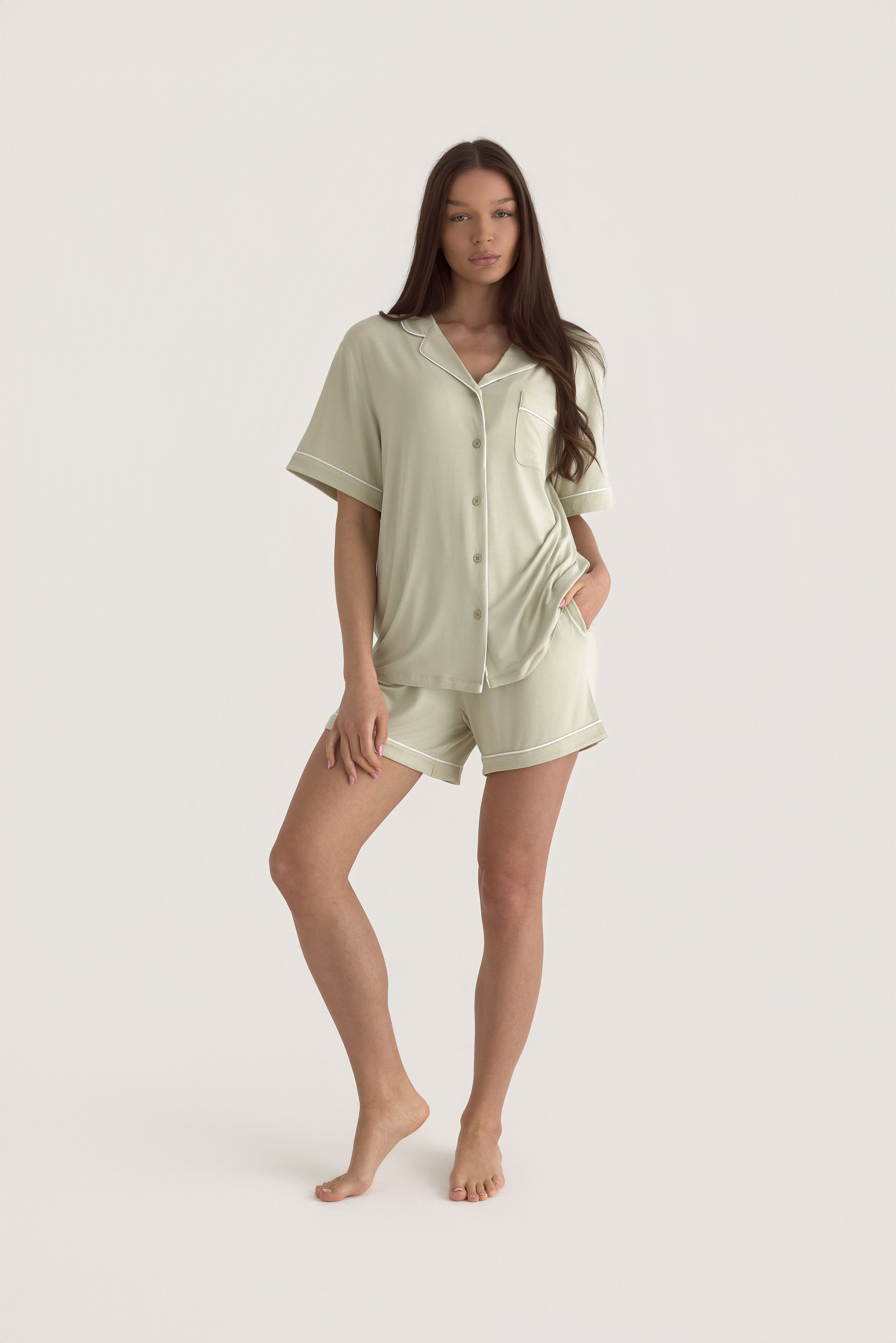 Muse Short PJs in Soft Sage: A woman models a comfortable sage green pajama set with short sleeves and shorts, featuring white piping detail.